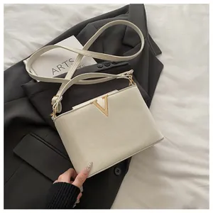 Detail of white leather shoulder bag featuring a gold V-shaped buckle on black blazer
