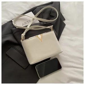 Cream shoulder bag with golden V-logo shown next to a smartphone for size reference