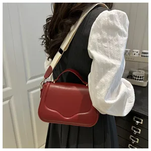 Detail of red leather crossbody bag with cream wide strap shown on model shoulder