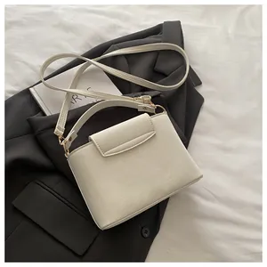 Detail of cream faux leather crossbody bag with gold hardware on a black blazer