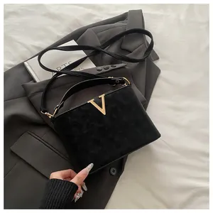 Close-up of black suede trapezoid handbag with gold V-shaped metal buckle detail