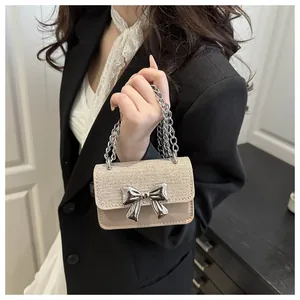 Detail of mini beige crossbody bag with woven flap, silver bow accent and chunky chain