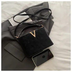 Detail of black matte handbag with golden V-logo placed on a stylish grey blazer