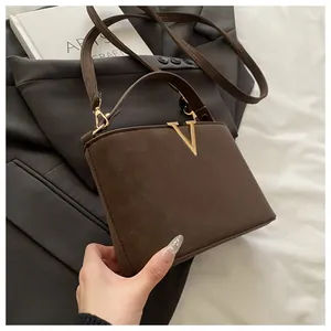 Close-up of brown textured leather bag featuring a gold V-shaped metal buckle and strap