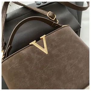 Detailed close-up of brown faux leather handbag featuring a gold V-shaped metal hardware