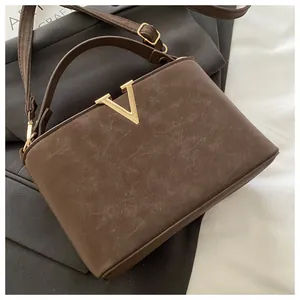 Macro shot of brown faux leather texture and gold V-shaped buckle on luxury crossbody bag