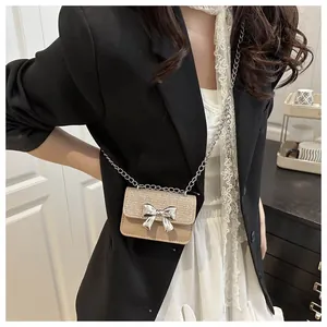 Mini crossbody bag with silver bow detail and chain strap worn by model in beige