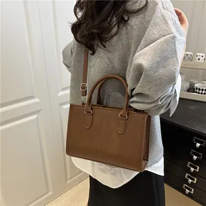 Brown cylinder handbag with vertical stripe embossing shown held by a model