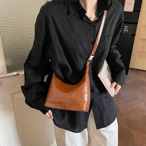 Chic brown glossy leather half-moon crossbody bag with embossed logo worn by a model
