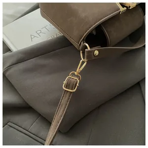 Detail of dark brown suede crossbody bag featuring a vintage gold T-bar buckle and texture