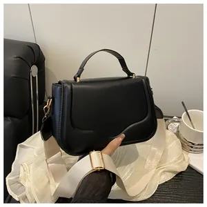 Detail of matte black crossbody bag with wide fabric strap and gold metal hardware