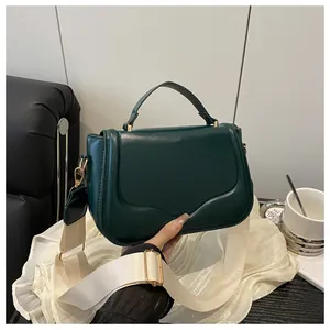 Detail of dark green leather handbag featuring gold hardware and a wide cream fabric strap