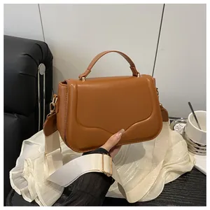 Close-up of caramel brown handbag with wave pattern flap and wide fabric strap