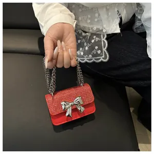 Detail view of red glitter handbag featuring a silver metal bow and chain handle