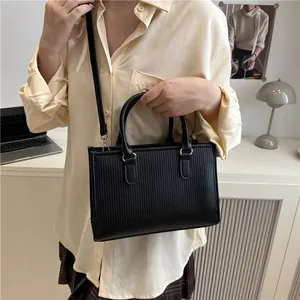Detail of black textured handbag showing vertical stripes and removable shoulder strap