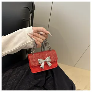 Detail of a mini red shoulder bag featuring a glittery flap and silver metal bow