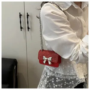 Detail of red glitter crossbody bag with silver bow buckle worn on person