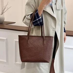 Deep brown woven tote bag for women with minimalist shoulder strap on model in trench coat
