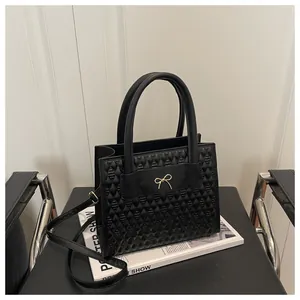 Detail of black quilted PU leather crossbody bag with golden metal bow and handle
