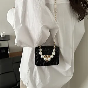 Woven black crossbody bag with pearl handle and metal heart clasp worn by model