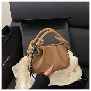 Brown pleated suede handbag with silver heart charm and braided tassel on gift box background