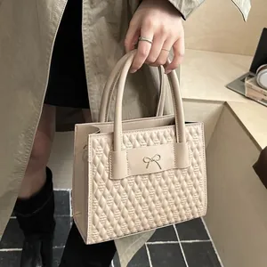 Elegant apricot quilted handbag with golden bow buckle and dual handles held by model