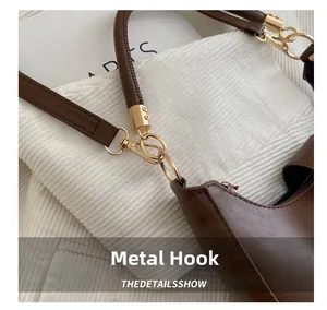 Close-up of golden hardware hooks and leather handles on brown crescent handbag