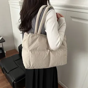 Beige quilted puffer tote bag with padded handles shown on model in a modern interior