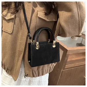 Detail of black leather crossbody bag with woven handle and gold hardware on model