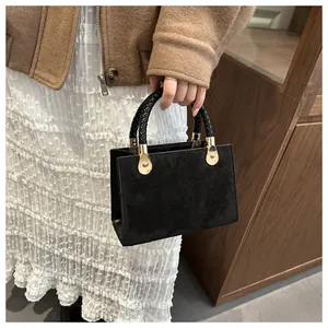 Detail of black crossbody bag featuring embossed clover patterns and woven handle