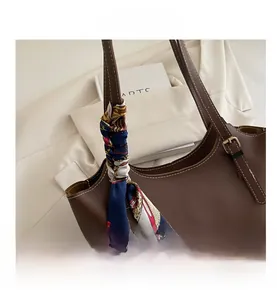 Detail view of brown tote bag featuring white contrast stitching and a silk scarf handle