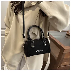 Détail du sac Boston en daim noir avec texte M'DoLnu et trench-coat beige élégant