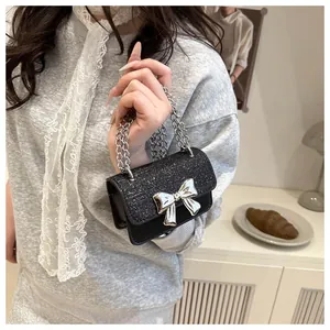 Detail of mini black crossbody bag with silver bow and glitter texture in indoor setting