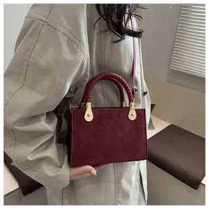Detail of burgundy crossbody bag with clover embossing and woven handle textures