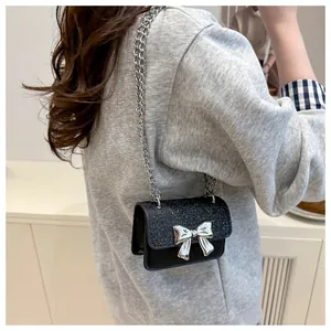 Rear view of a model wearing the mini black glitter crossbody bag with silver bow accent