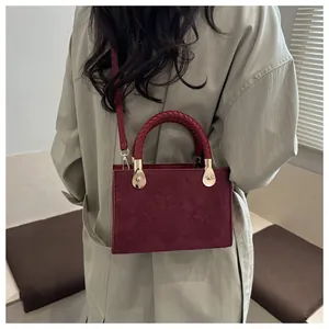 Detail of burgundy crossbody bag with clover embossing and woven handle on model