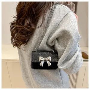 Close-up of black mini chain bag featuring a glittery flap and large silver metal bow detail