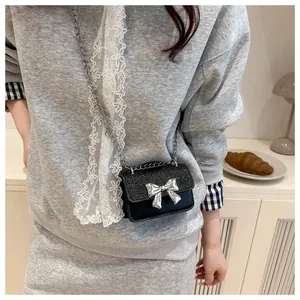 Detail of a mini black sequin crossbody bag with a silver metal bow accent