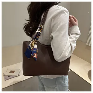 Detail of a large brown leather tote bag with a decorative floral silk scarf on the handle