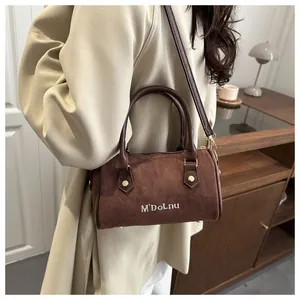 Détail d'un sac cylindrique en daim marron avec broderie de lettres et accents dorés
