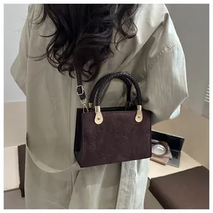 Detail of dark brown crossbody bag with clover embossing and woven top handle on model