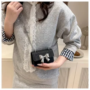 Detail of a mini black crossbody bag with sequin texture and a silver bow decoration