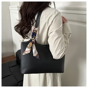 Detail of a minimalist black tote bag featuring a decorative printed silk scarf on the handle