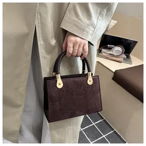 Detail of dark brown handbag with clover embossing and woven handle on desk