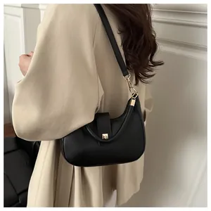 Close-up of black leather crescent bag with gold twist-lock on stylish beige suit