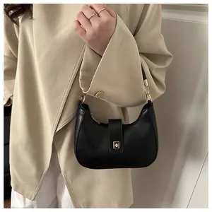 Detail of black crescent hobo bag with gold metal clasp and chain held by a person