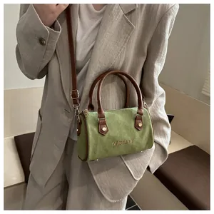 Sac Boston en daim vert avec poignées marron porté par un mannequin en tailleur