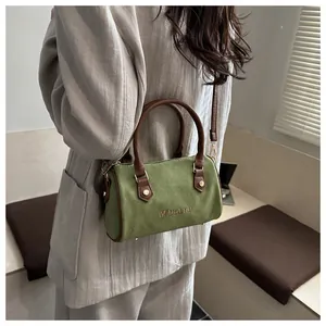 Détail du sac Boston en daim vert avec poignées en cuir marron et finitions dorées