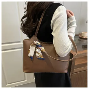 Detailed side view of a brown tote bag featuring white stitching and a silk scarf handle wrap