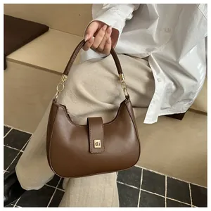 Detail of a brown leather crescent shoulder bag featuring gold-tone metal hardware